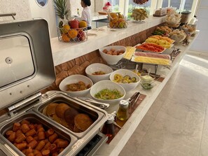 En buffet med et udvalg af mad, herunder frugt, grøntsager, kød og bagværk.
