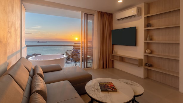A modern hotel room with a balcony, a sofa, a round table, and a flat-screen TV.
