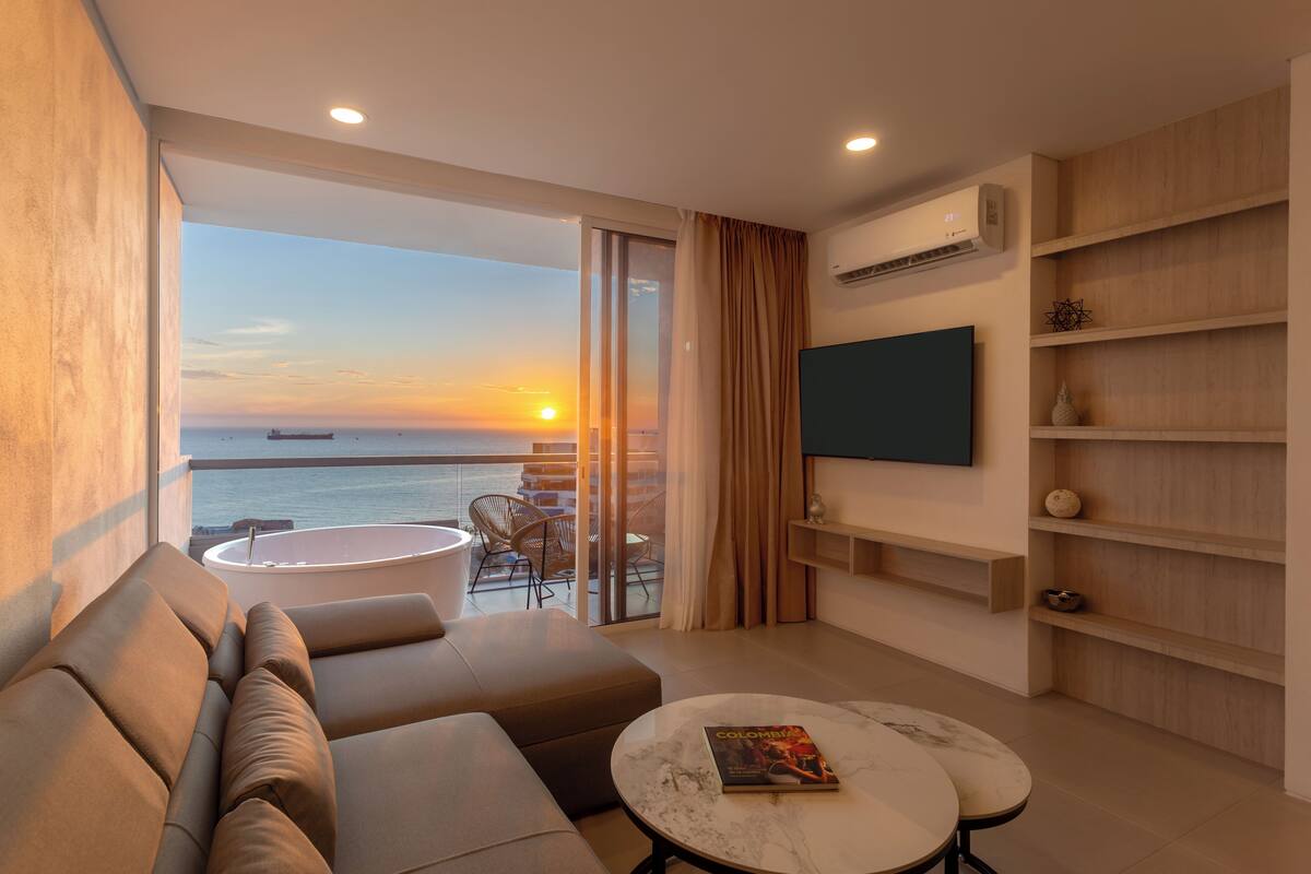A modern hotel room with a balcony, a sofa, a round table, and a flat-screen TV.
