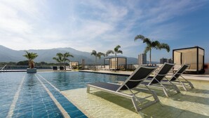 A pool area with lounge chairs and palm trees, with mountains in the background.