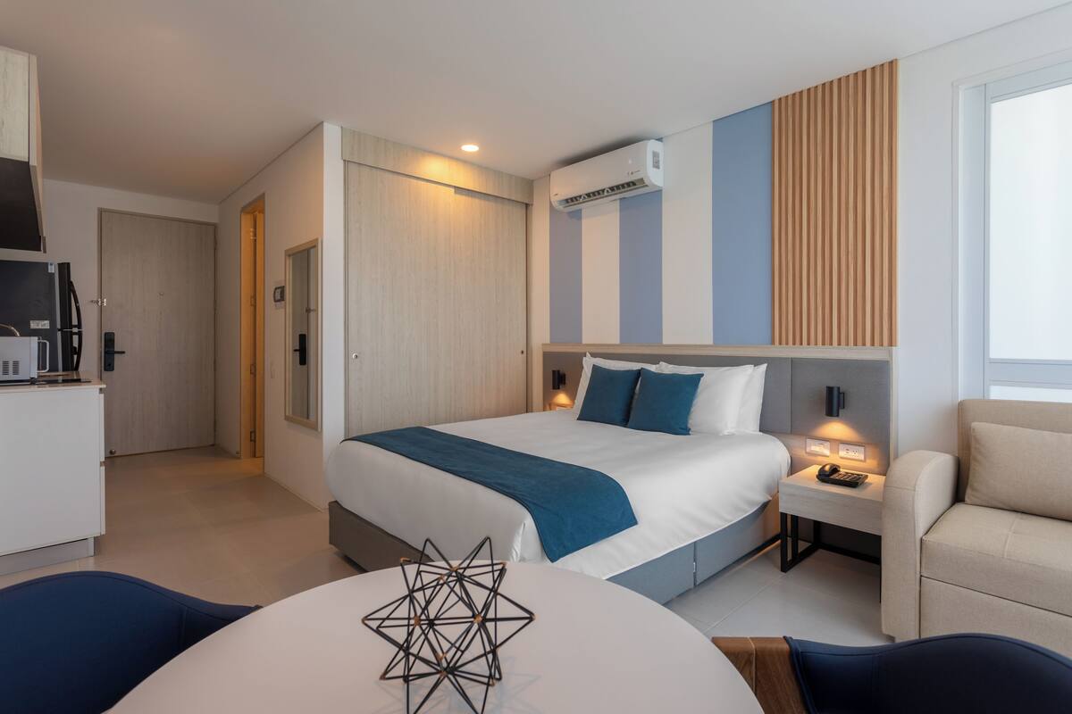 A modern hotel room with a large bed, bedside table, and a small desk.