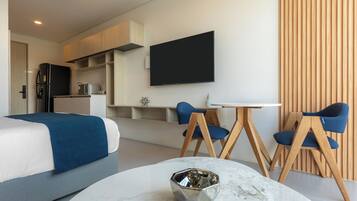 Una habitación de hotel moderna con cama, mesa de comedor con sillas, televisor montado en la pared y zona de cocina.