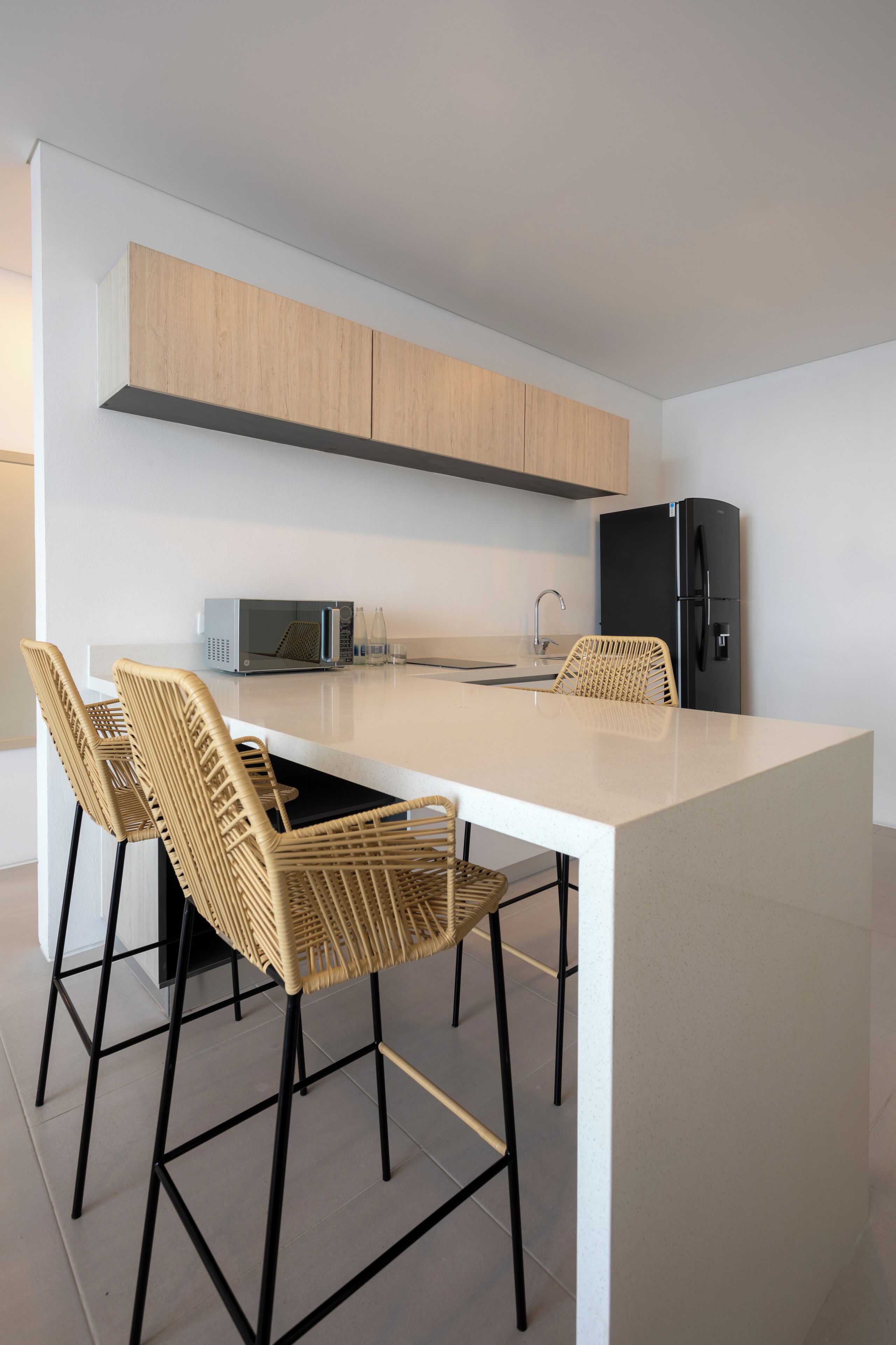 A modern kitchen with a white island, black chairs, a black refrigerator, and a microwave.