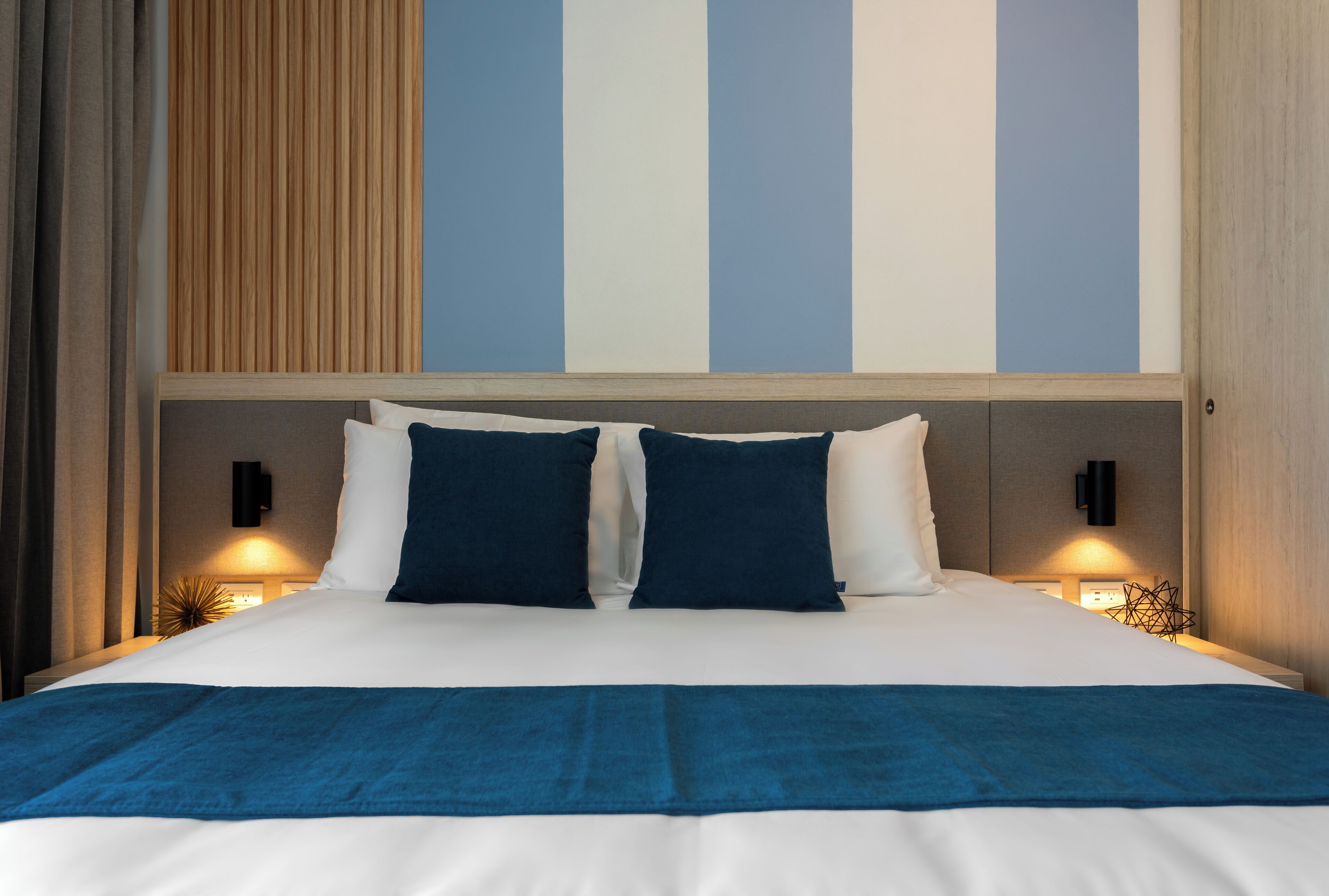 A hotel room with a large bed, two bedside tables, and a wall with vertical stripes.