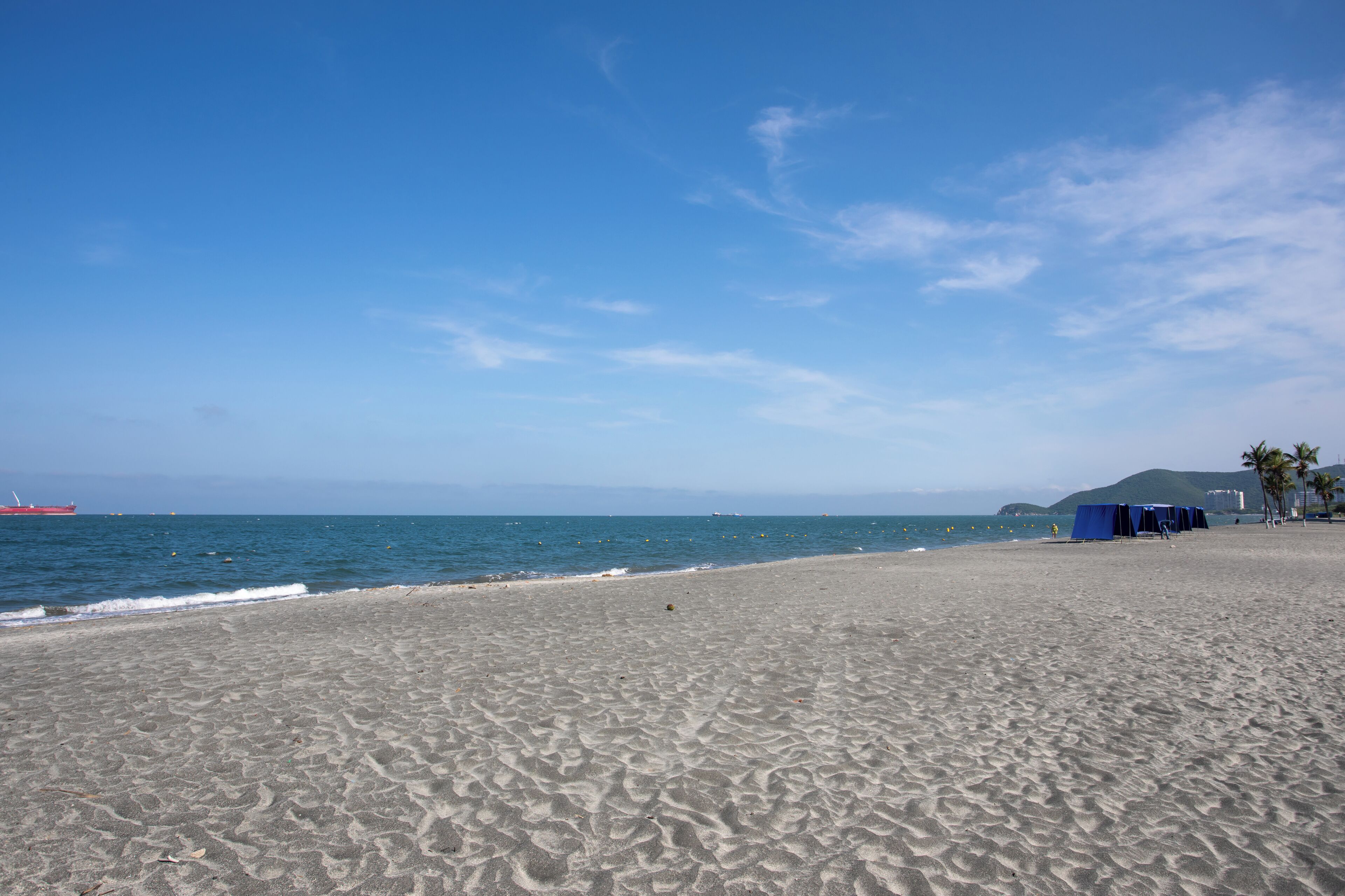 Una spiaggia con una battigia sabbiosa, alcune tende e una nave all'orizzonte.
