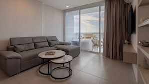 A modern living room with a grey sofa, a round coffee table, and a large window with a view of the sea.