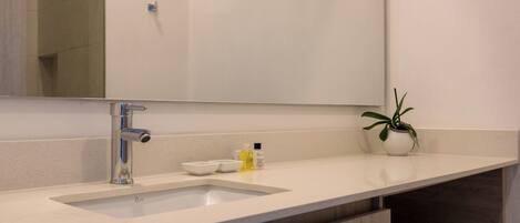 A modern bathroom with a large mirror, a sink, and a potted plant.