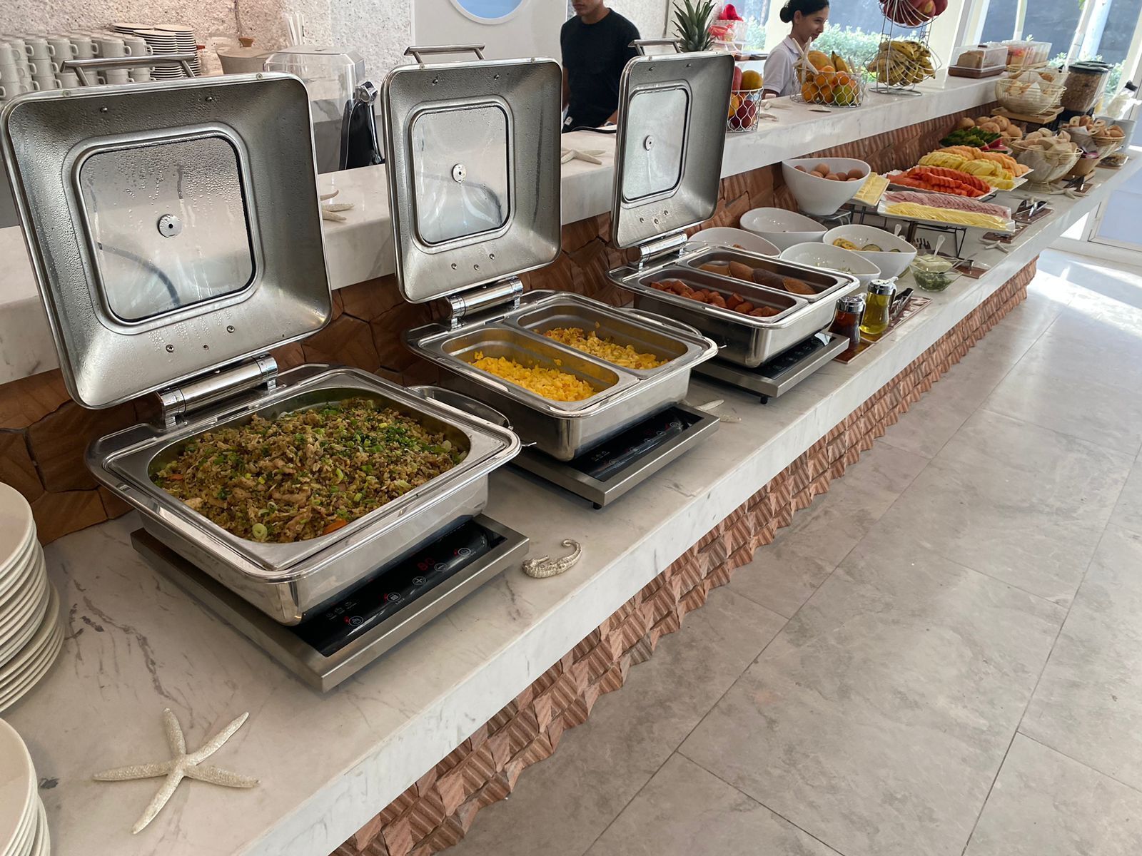 A buffet with various food options, including fried rice, yellow rice, and other dishes in metal containers.