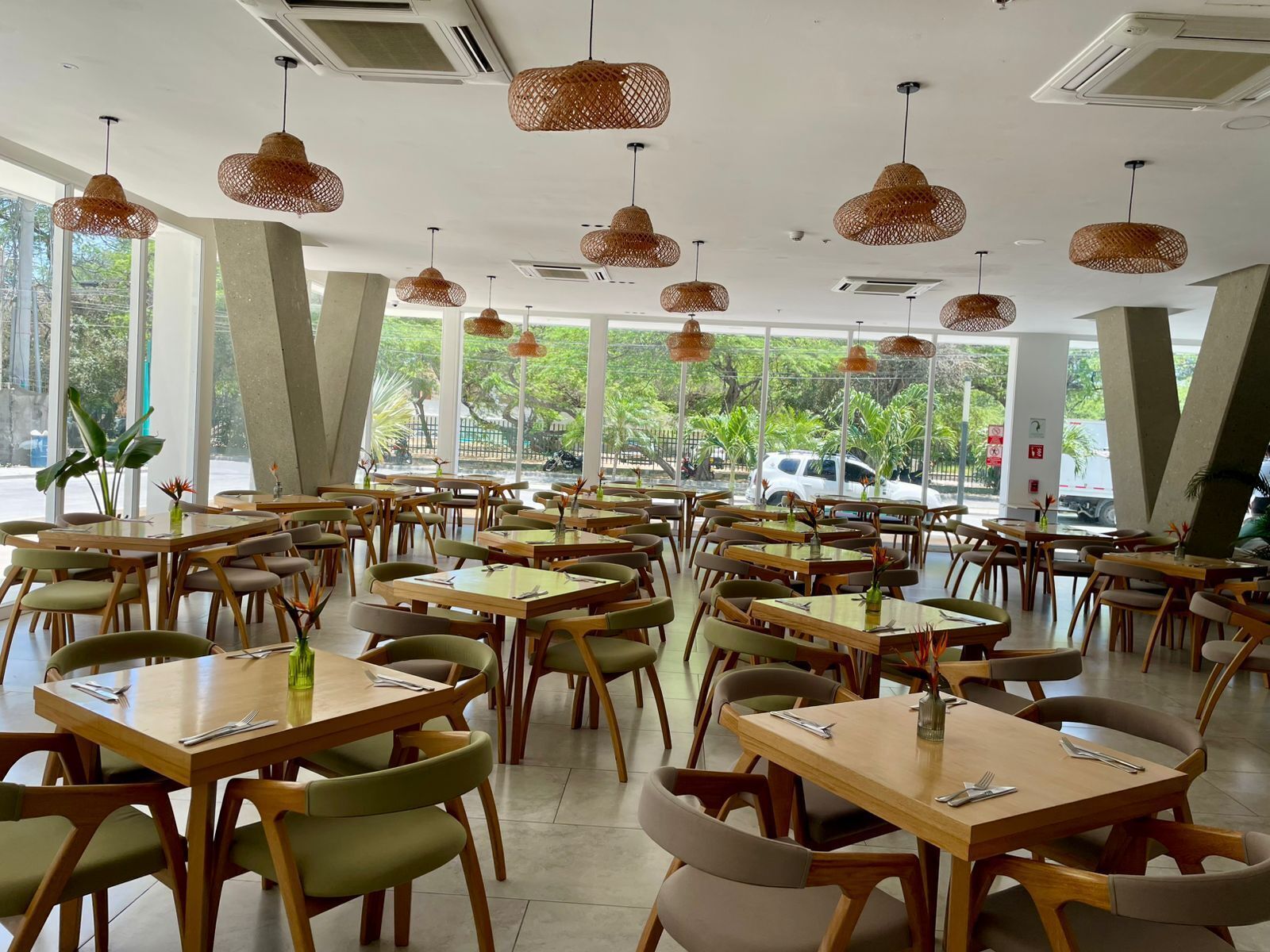 A spacious restaurant with multiple tables and chairs, large windows, and hanging wicker lamps.
