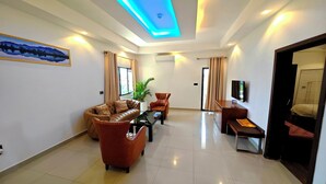 A modern living room with a sofa set, a coffee table, and a TV on a stand. - Soluxe Hotel Cotonu (Cotonou)