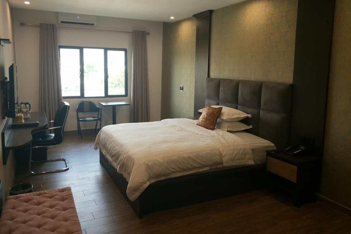 A modern hotel room with a large bed, a desk with a chair, a small table, and a window with curtains.