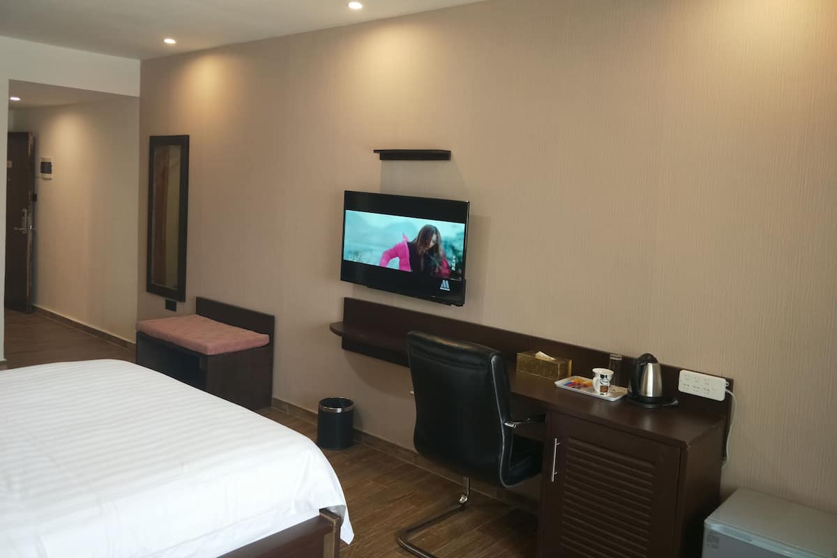 A hotel room with a bed, a desk, a chair, a television, and a minibar.