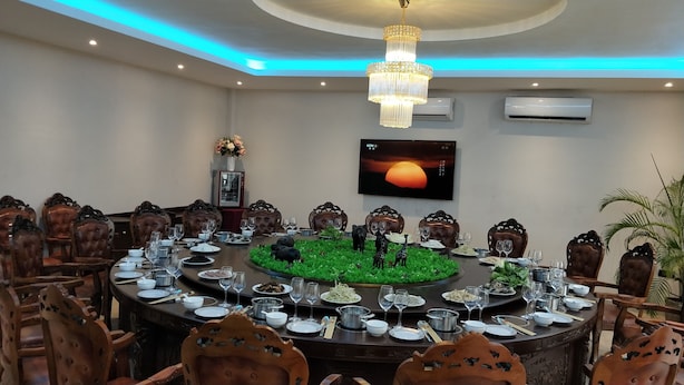 A round dining table with chairs, a chandelier, and a TV on the wall. - Soluxe Hotel Cotonu (Cotonou)