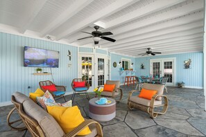 Un espacio de estar al aire libre techado con muebles de mimbre, una mesa redonda y ventiladores de techo.