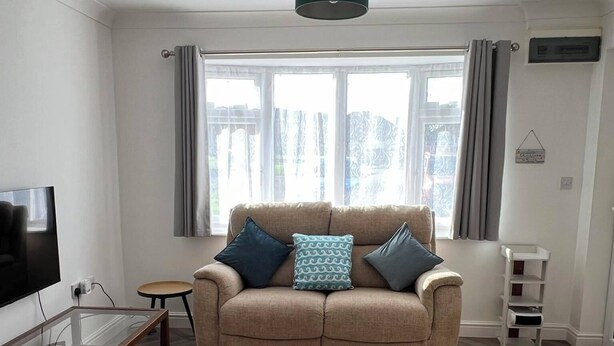 Un salon moderne avec un canapé beige, un tapis à motifs et un téléviseur posé sur une table en verre.