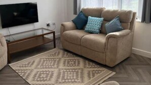 Un salon avec un canapé beige, un téléviseur à écran plat et un tapis à motifs.