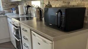 Une cuisine compacte équipée d’un four à micro-ondes, d’une bouilloire et d’appareils électroménagers en acier inoxydable.