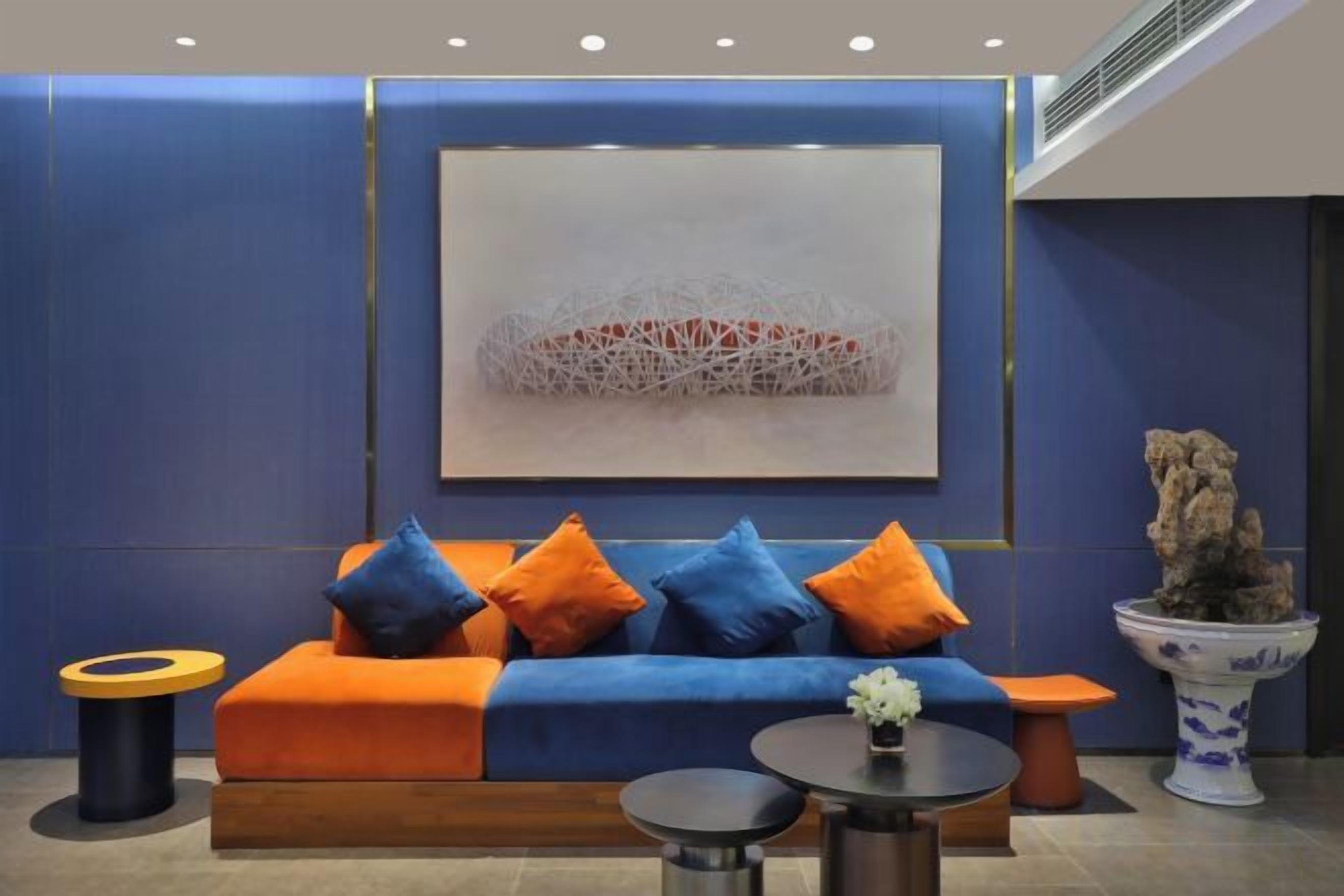 A modern lounge area with a blue sofa, orange cushions, a round table, and a decorative plant.