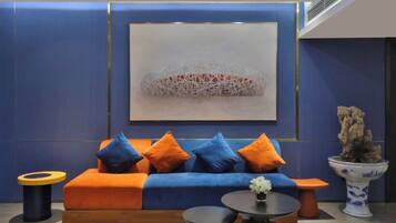 A modern lounge area with a blue sofa, orange cushions, a round table, and a decorative plant.