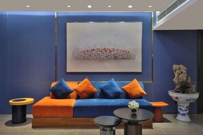 A modern lounge area with a blue sofa, orange cushions, a round table, and a decorative plant. - Orange Hotel (Beijing Asian Games Village, Bird's Nest) (Beijing)