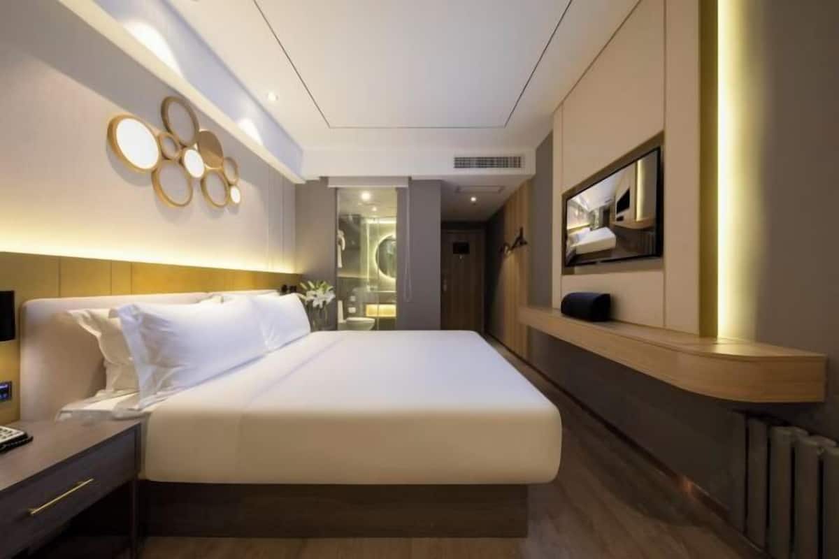 A modern hotel room with a large bed, a bedside table, a mirror, and a television.