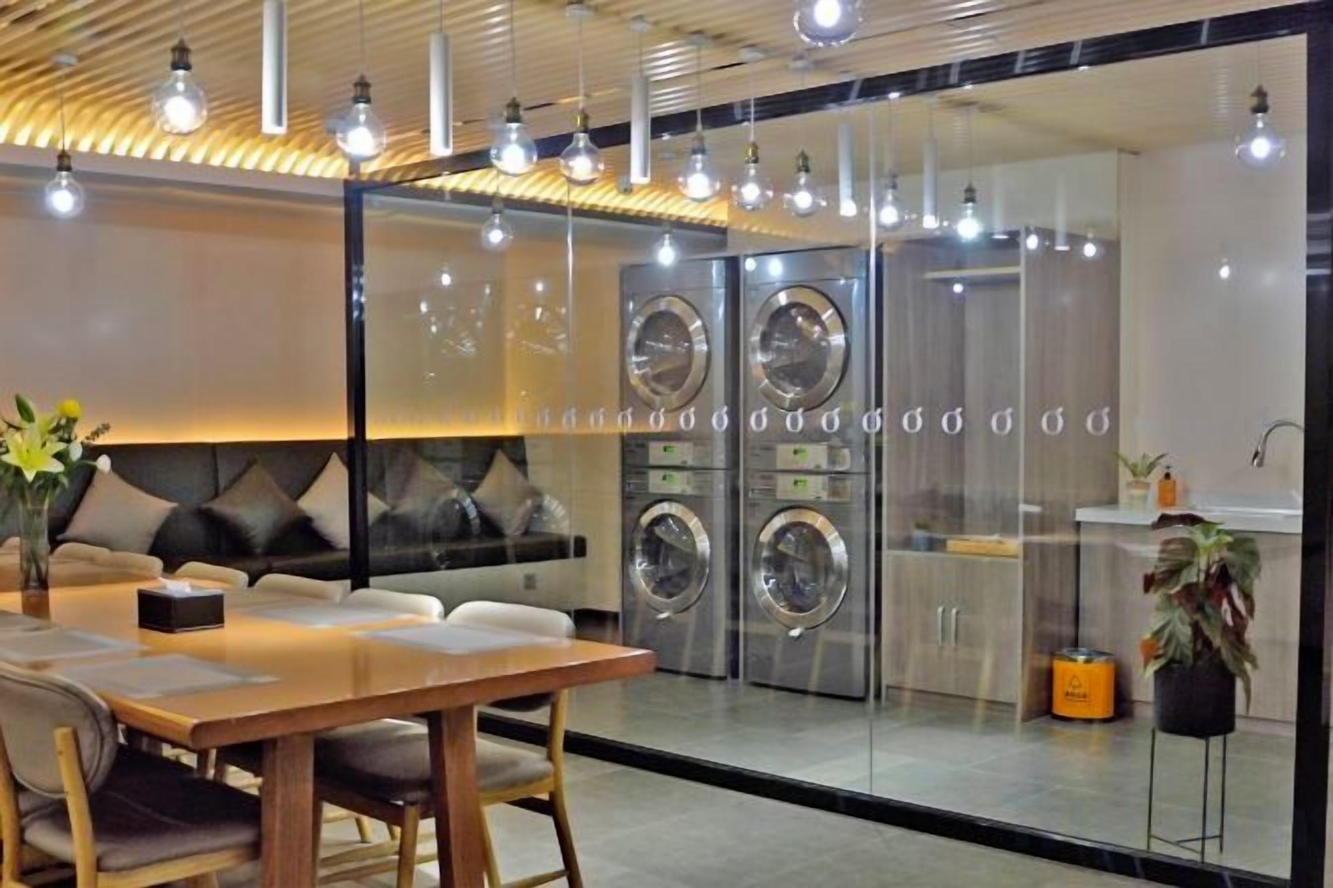A modern room with a wooden table, chairs, a sofa, and a large window with a view of a laundry area.