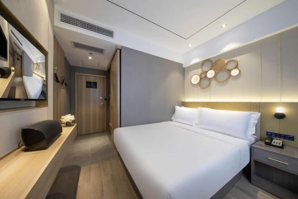 A modern hotel room with a large bed, a bedside table, a flat-screen TV, and a wall-mounted light fixture.