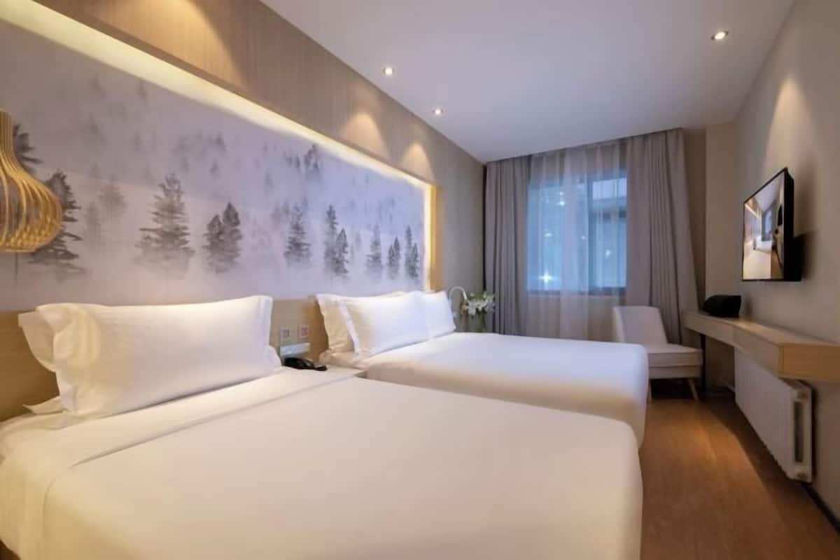 A hotel room with two beds, a desk, a chair, a television, and a large window with curtains.