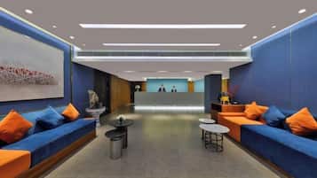 A modern lobby with blue sofas, orange cushions, a reception desk, and a large abstract artwork on the wall.