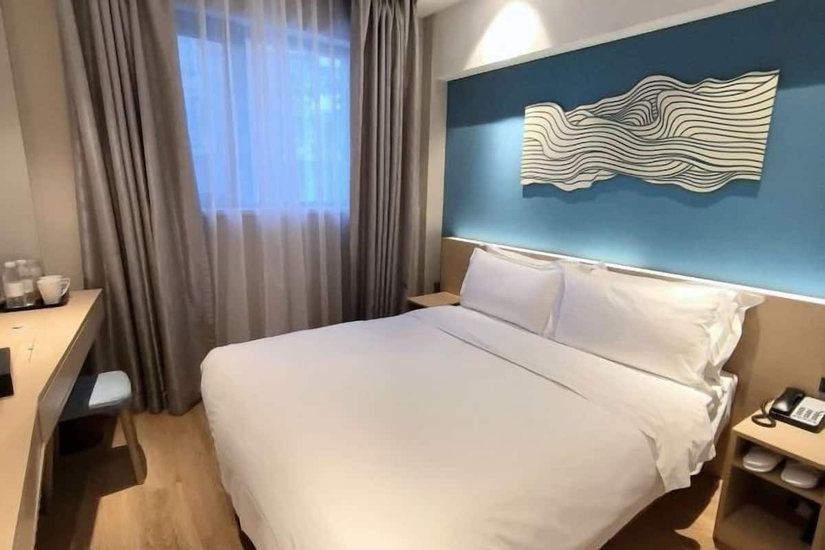 A hotel room with a bed, a desk, a chair, a phone, and a wall art piece.