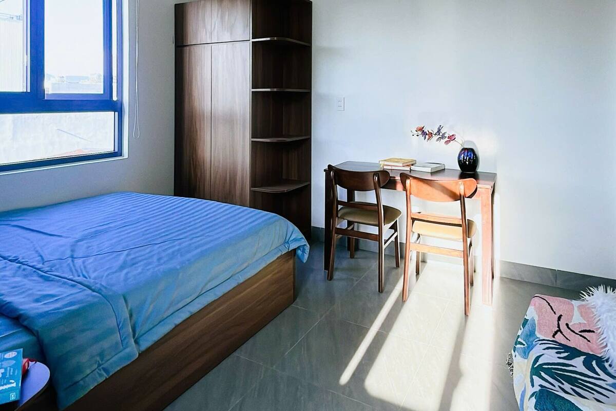 A bedroom with a bed, a wardrobe, a desk with a chair, and a window.