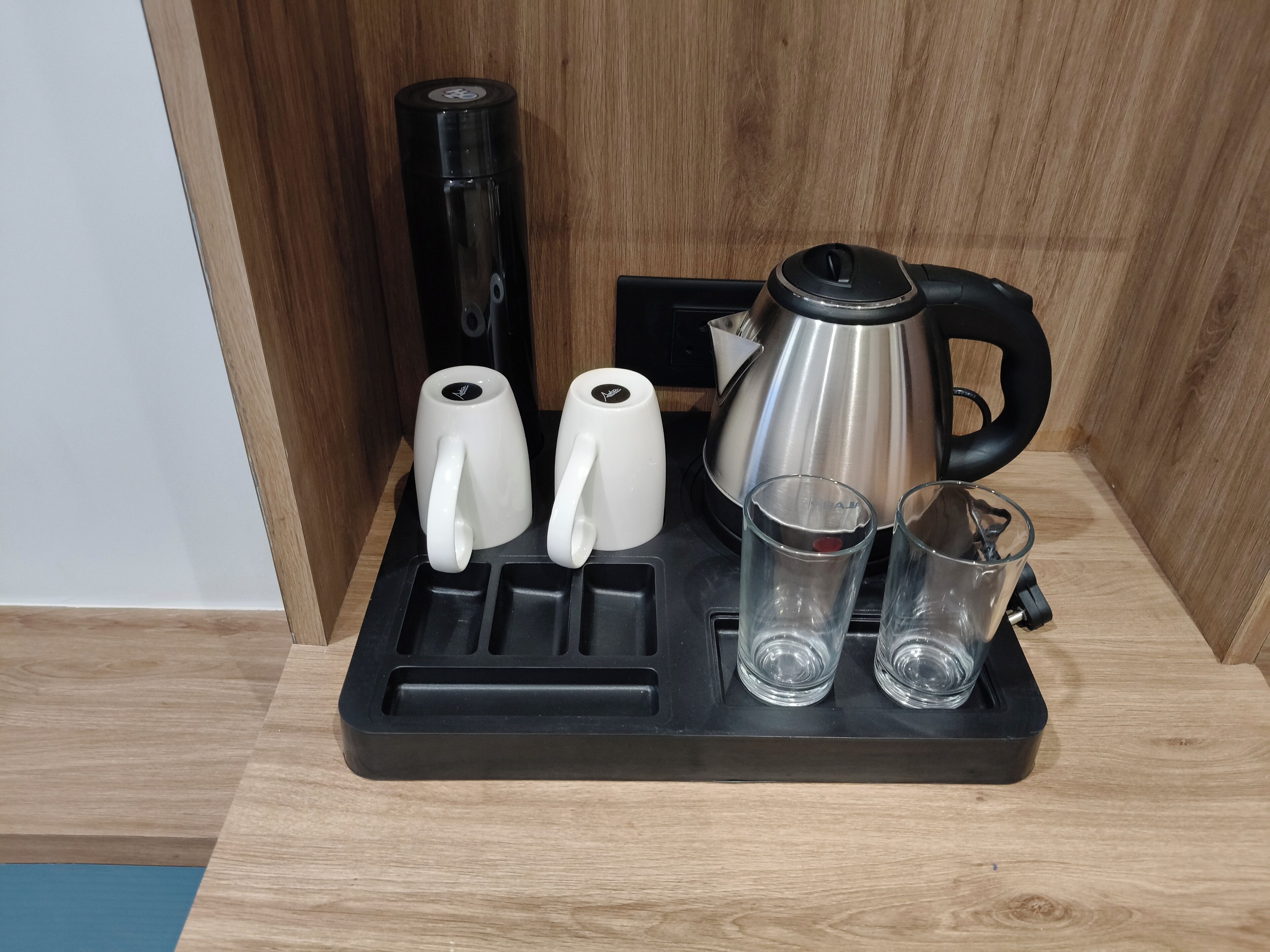 A coffee station with a kettle, two white mugs, and two glasses on a tray.
