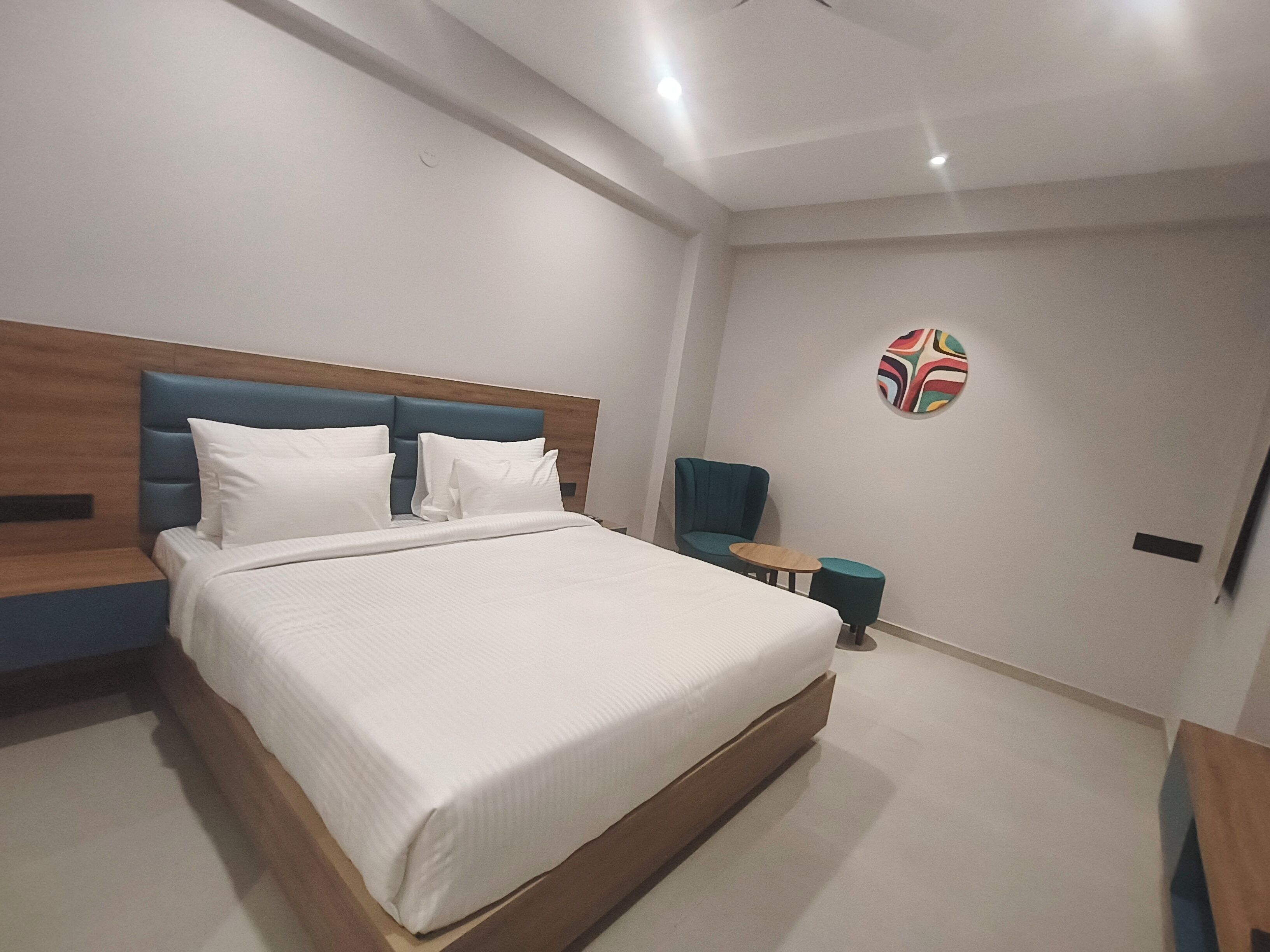 A modern hotel room with a large bed, a wooden headboard, a small round table, and a blue chair.