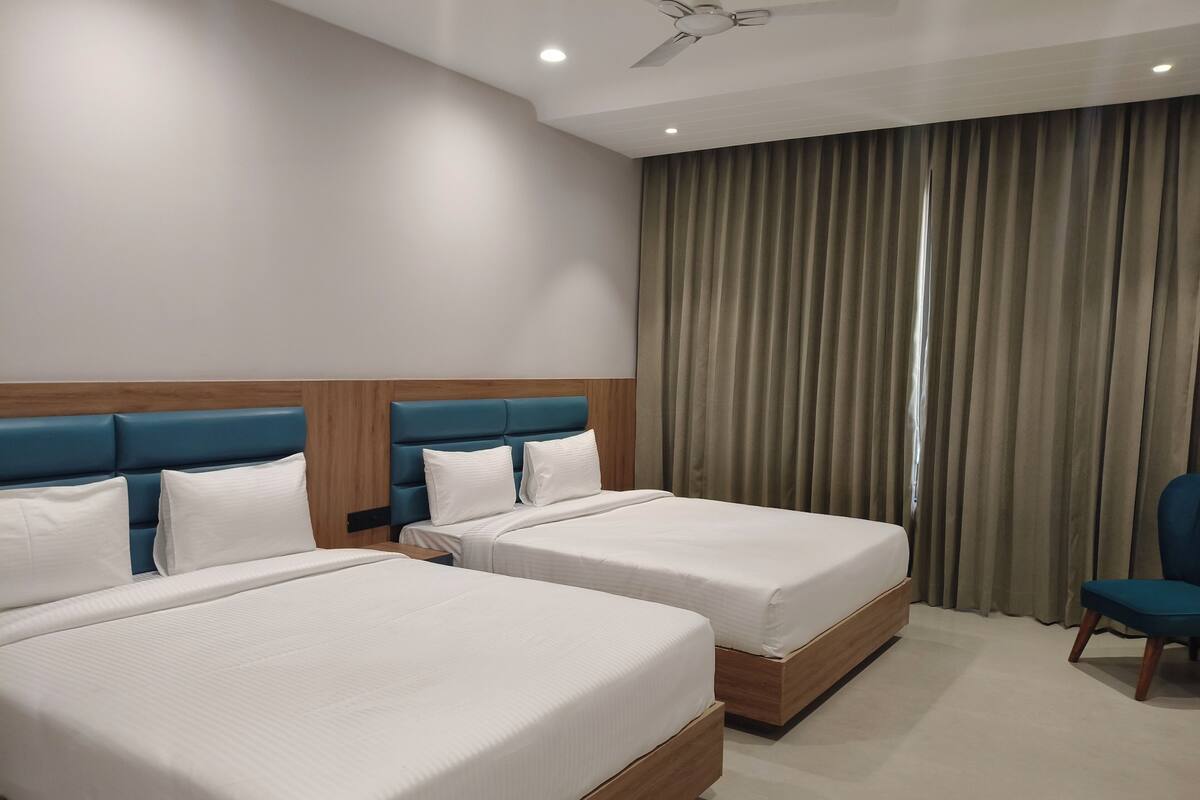 A hotel room with two beds, a ceiling fan, and a large window with curtains.