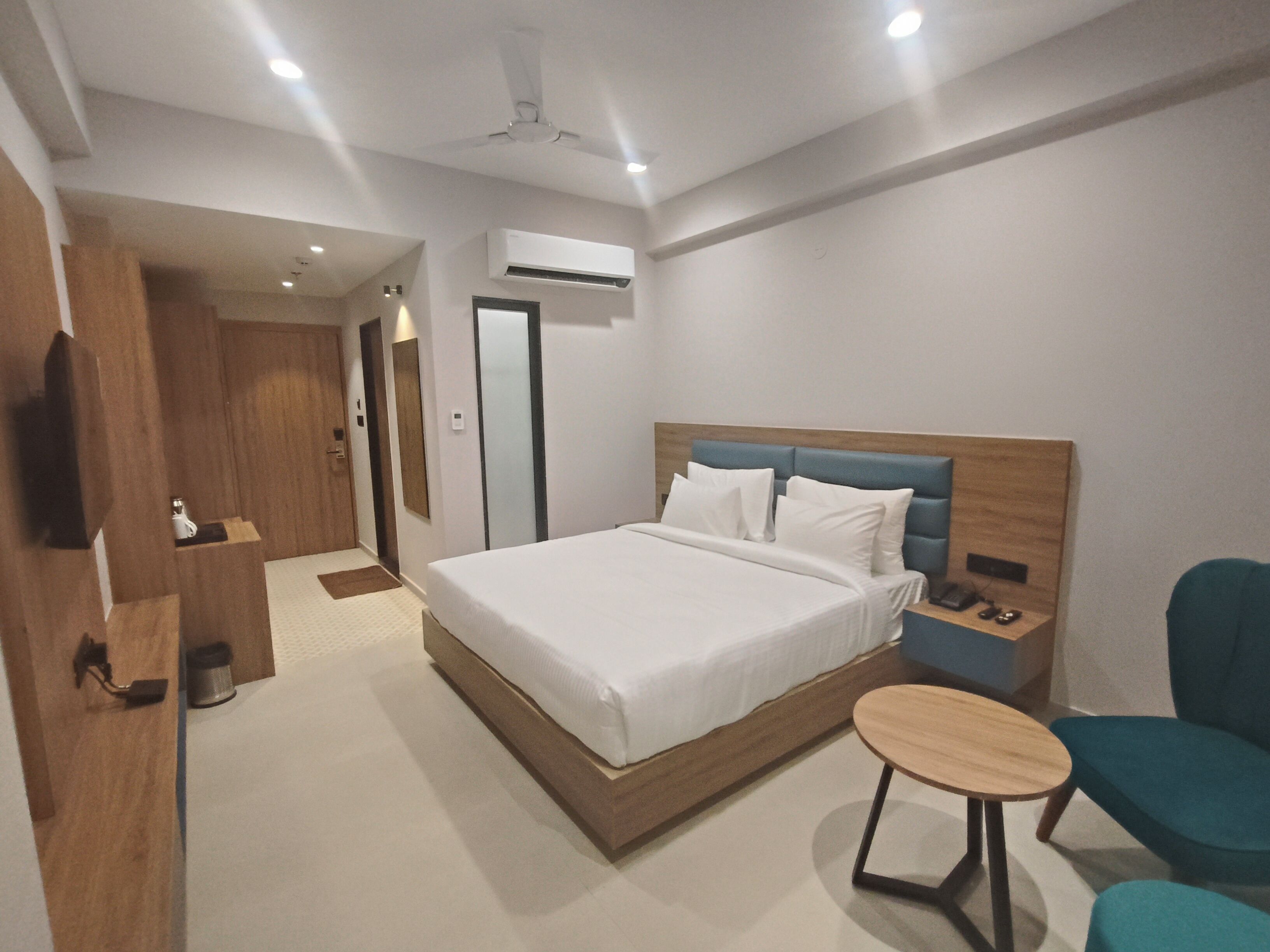 A modern hotel room with a large bed, a bedside table, a chair, and a small table.