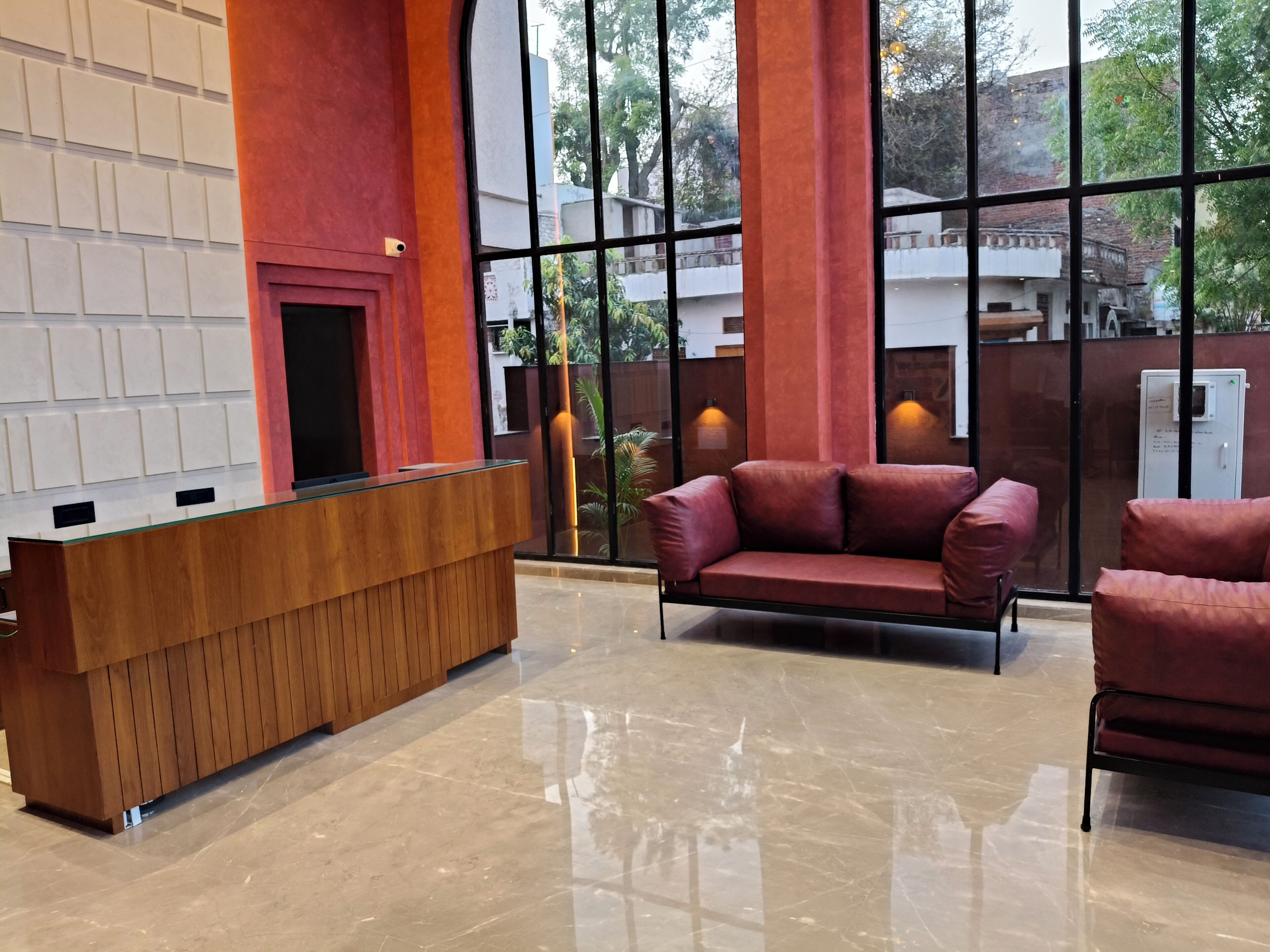 Un área de recepción con un mostrador de madera, un sofá rojo y grandes ventanales que ofrecen vistas al exterior.