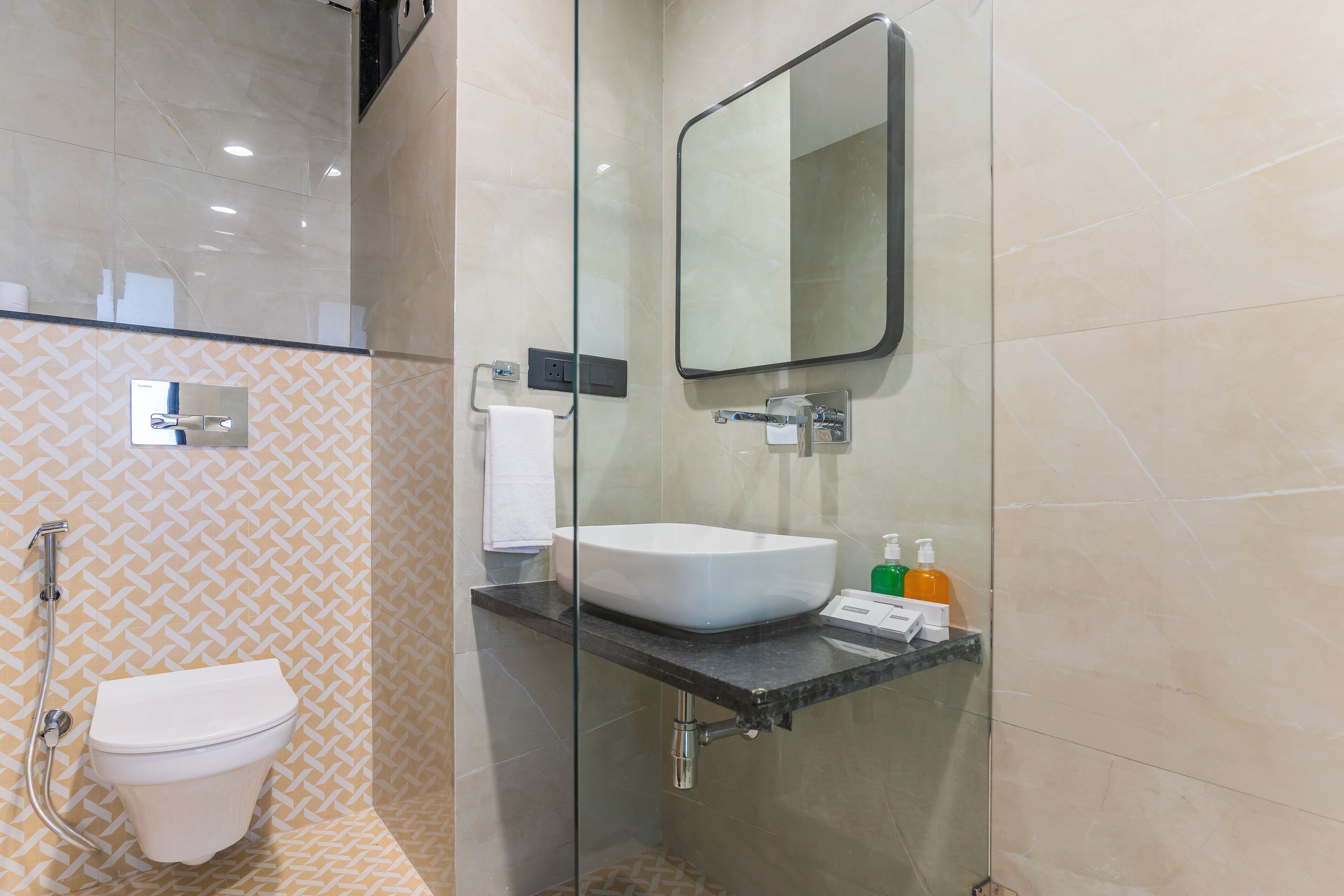 Une salle de bain moderne avec une douche à l’italienne en verre, des toilettes blanches, un lavabo avec un miroir au-dessus et des articles de toilette posés sur le comptoir.