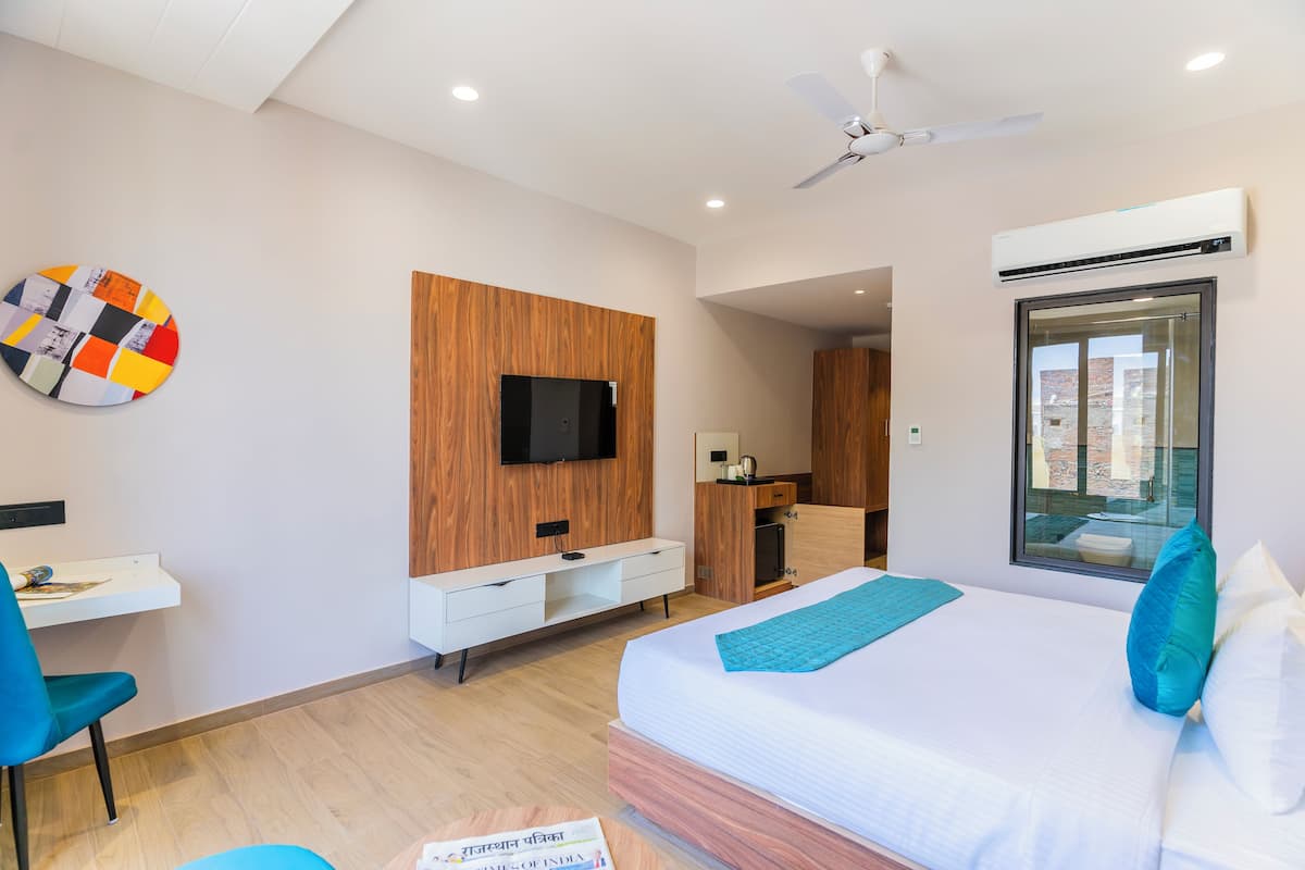 A modern hotel room with a bed, a desk, a TV, and a window.