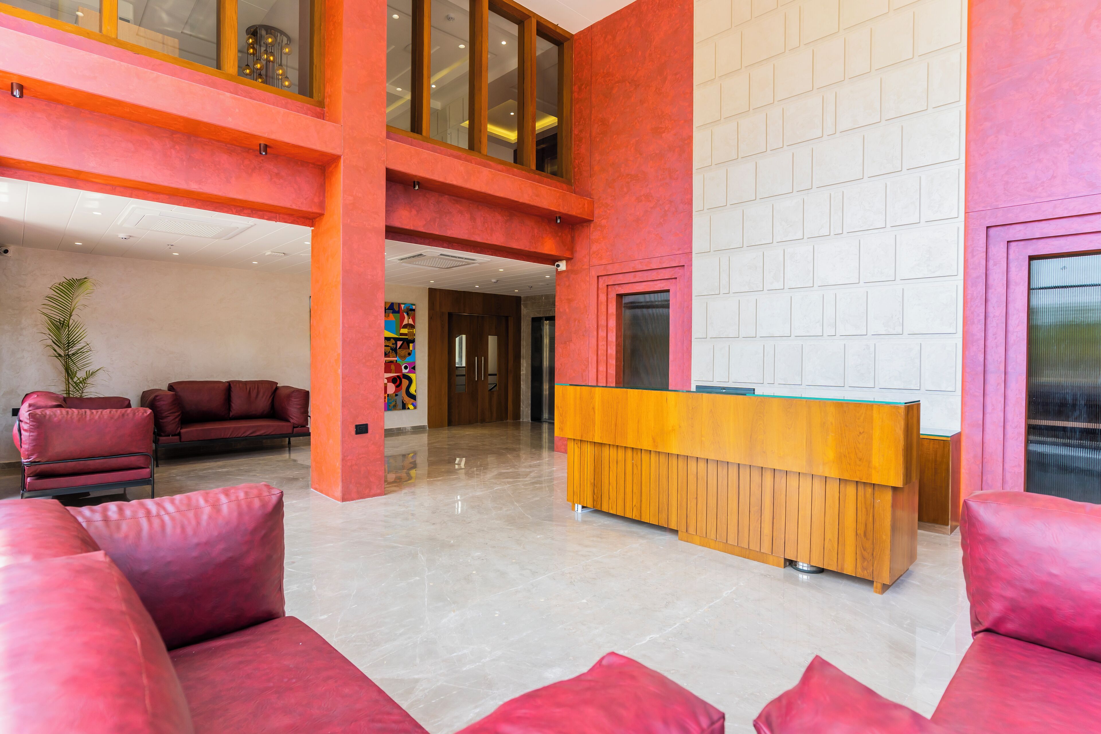 Un vestíbulo amplio con una mesa de recepción, sofás rojos y una planta grande en maceta.