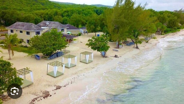 Ein Objekt direkt am Strand mit mehreren Häusern, einem Sandstrand und üppiger Vegetation.