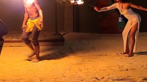 Eine Person führt eine Feuershow auf, wobei eine Fackel auf dem Kopf balanciert wird, während eine andere Person eine brennende Fackel hält.