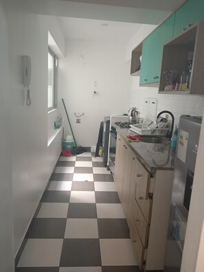 Una cocina estrecha con piso a cuadros, una ventana y servicios básicos.