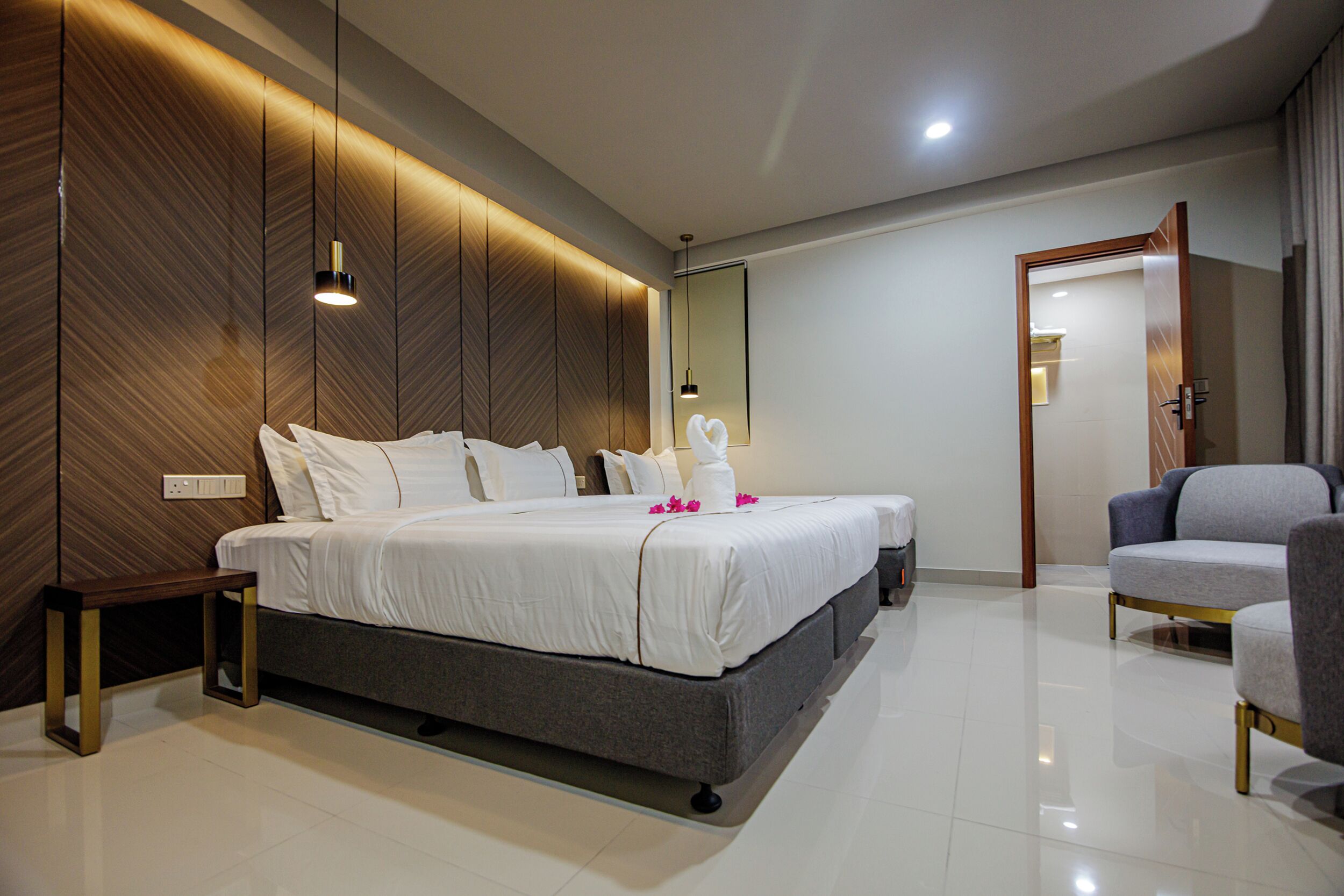 A modern hotel room with a large bed, a bedside table, a chair, and a mirror.