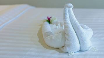 Una cama bien hecha con una toalla blanca dispuesta en forma de cisne, acompañada de una pequeña flor.