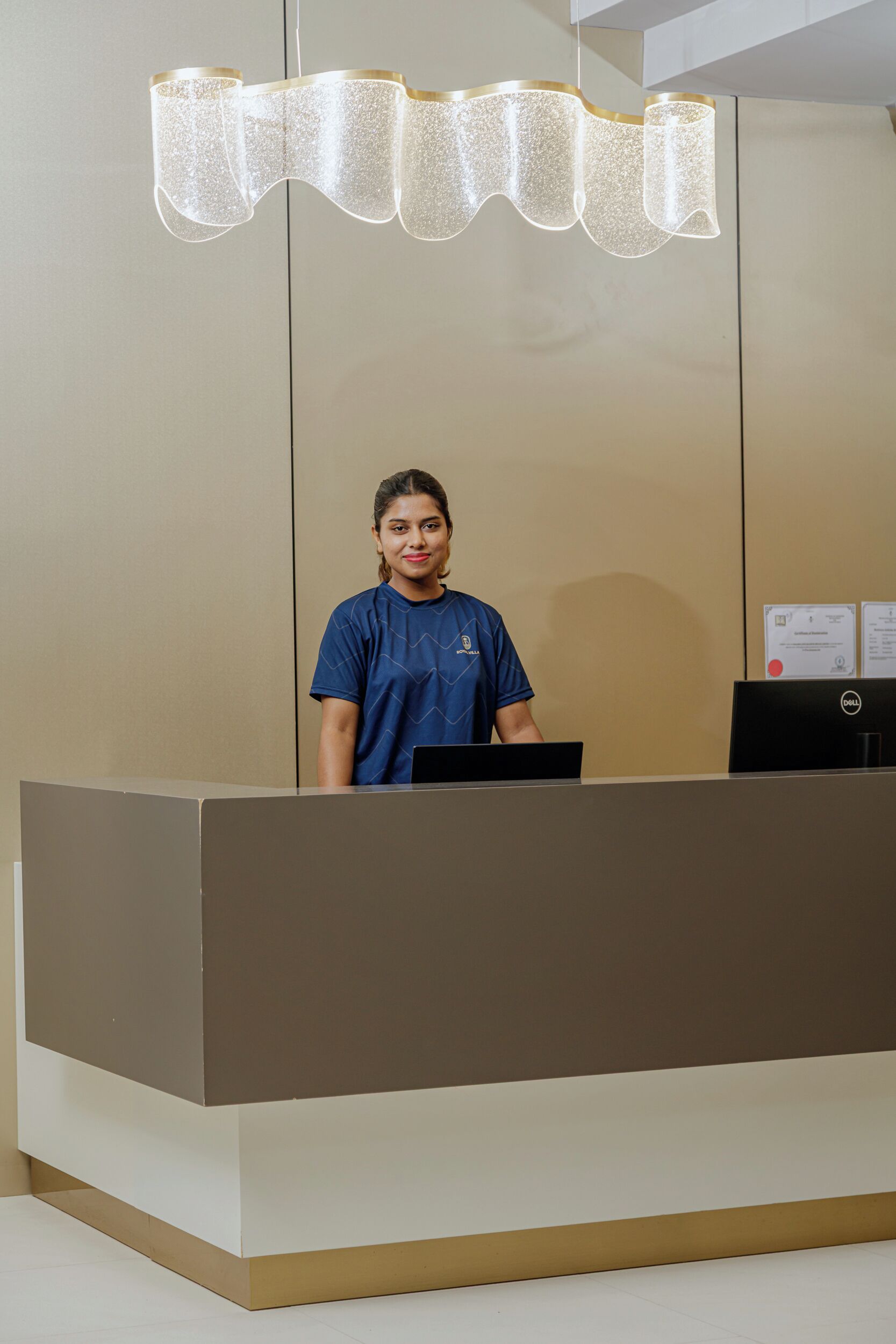A reception desk with a modern design, a person standing behind it, and a unique chandelier above.