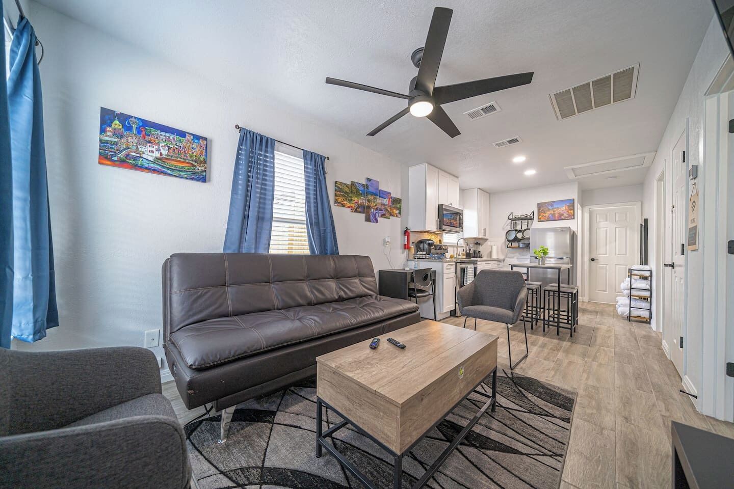 A living room with a sofa, a coffee table, and a TV. There is a kitchen area with a dining table and chairs.