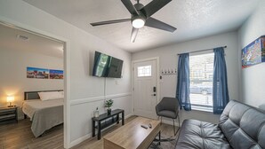 Ett modernt rum med en säng, en soffa, en tv, en takfläkt och ett fönster med gardiner.