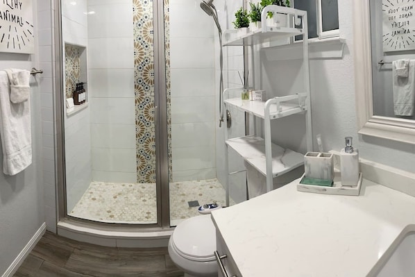 A modern bathroom with a glass shower enclosure, white tiled walls, and a marble countertop.