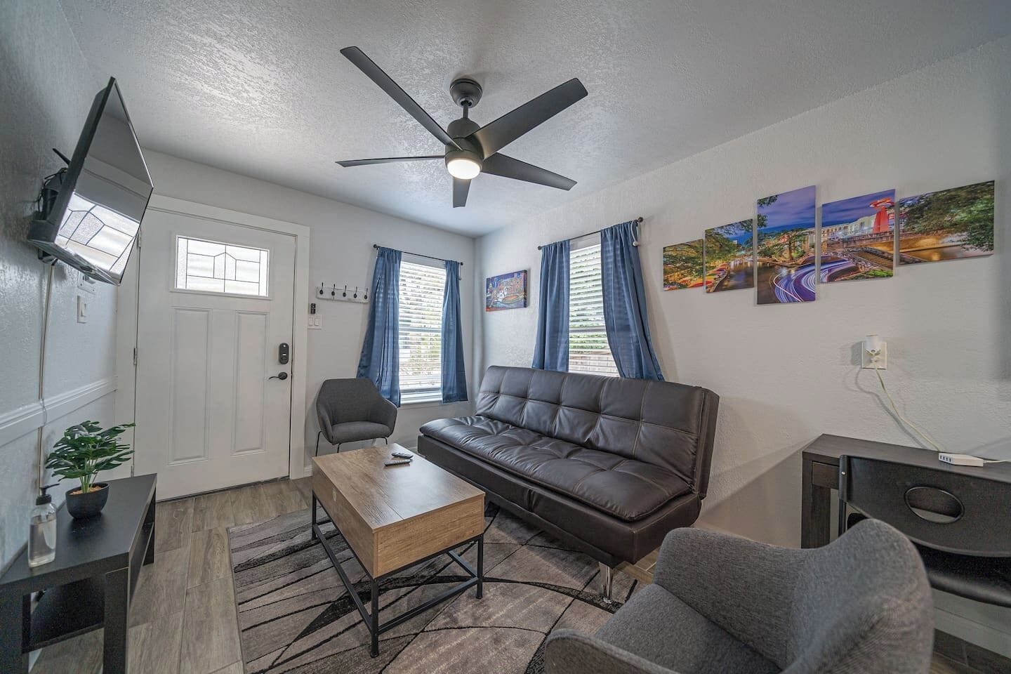A living room with a sofa, armchair, coffee table, ceiling fan, TV, and artwork on the wall.