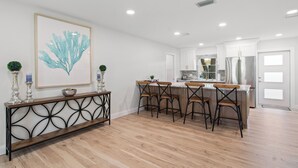 Une cuisine moderne avec des meubles blancs, un réfrigérateur en acier inoxydable et une table à manger en bois, accompagnée de quatre chaises.